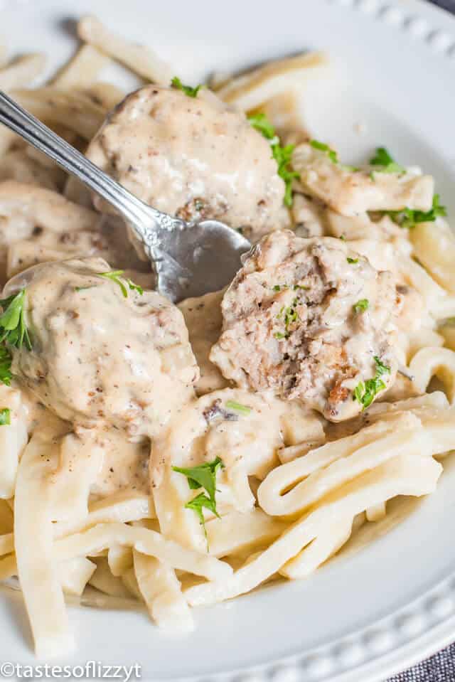This homemade Swedish meatballs recipe will give Ikea Swedish meatballs a run for their money! The from-scratch pan gravy has a delicious creamy flavor. These are the best meatballs for a classic comfort food dinner recipe. homemade Swedish meatballs on a bed of egg noodles. One meatball has been cut in half with a fork
