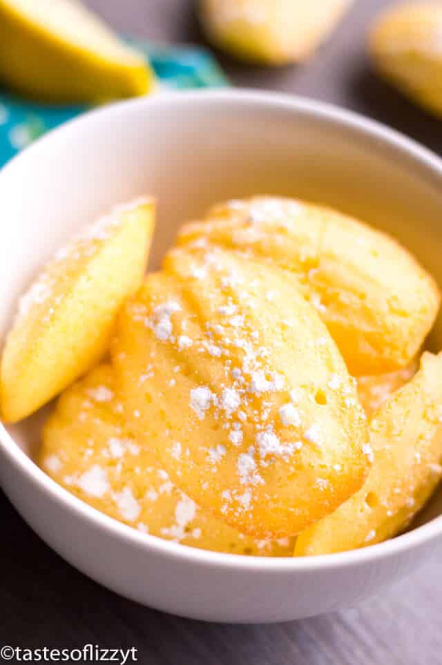 Lemon madeleine cookies are delicious cake-like cookies with a crispy exterior and soft interior. This madeleines recipe pairs perfectly with coffee or tea. #madeleines #cookierecipes lemon madeleines dusted with powdered sugar