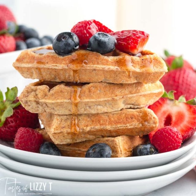 a stack of 4 whole grain waffles with berries and syrup