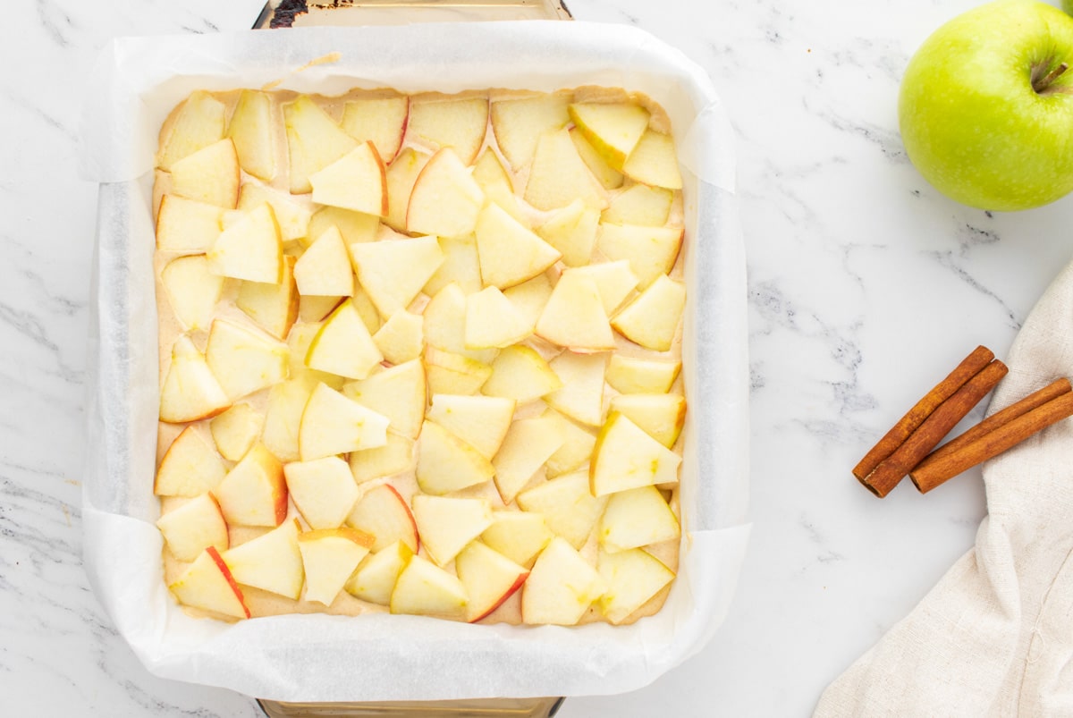sliced apples over cheesecake batter in a pan