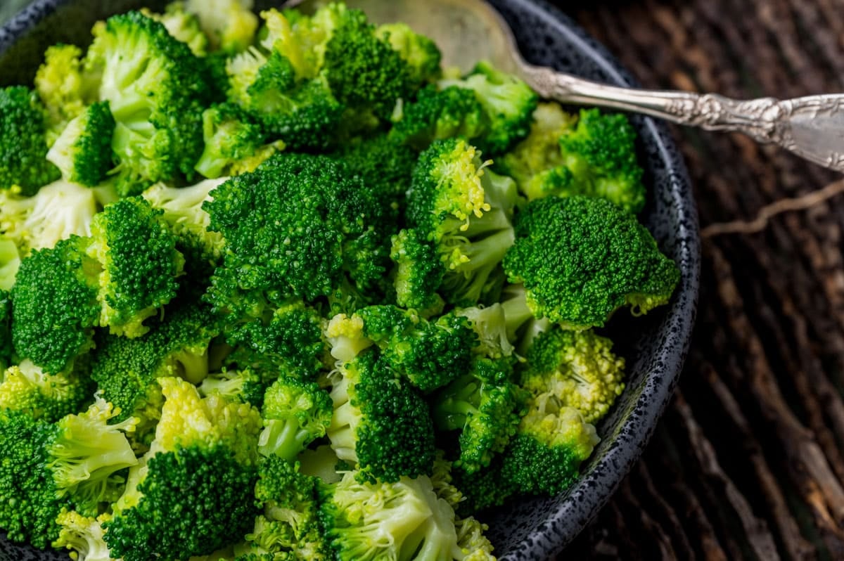 closeup of steamed broccoli in a black bowl with a spoon