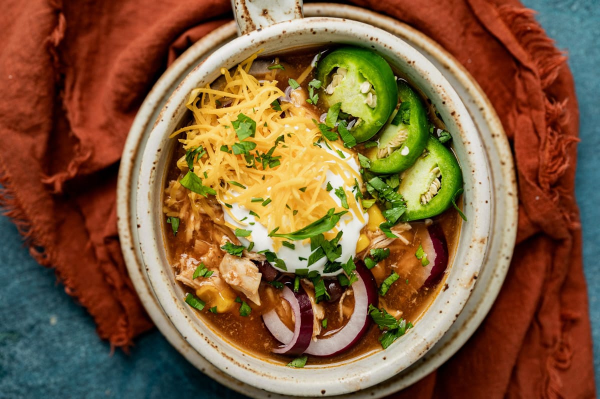 a bowl of bbq chicken soup with cheese, jalapeno and onion