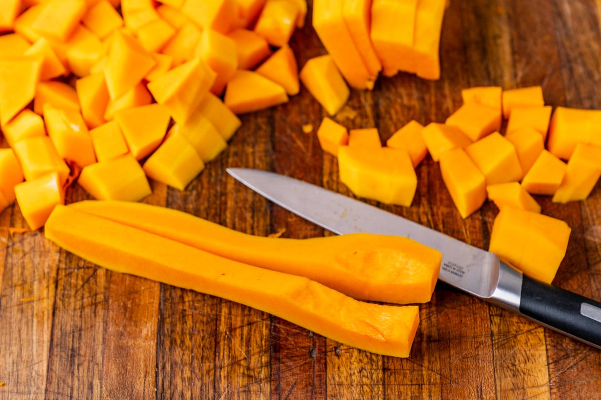 butternut squash cut in pieces on a cutting board with a knife