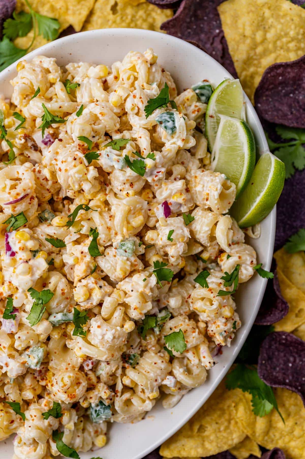 a plate of street corn pasta salad with tortilla chips and limes