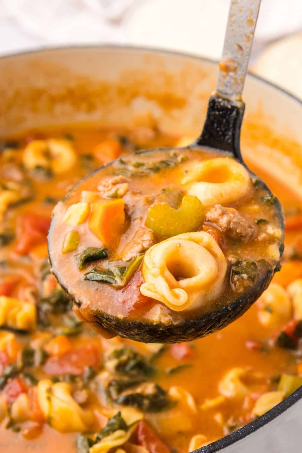 a ladle full of cheese tortellini soup with italian sausage