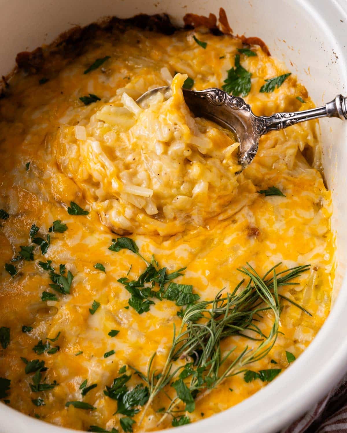 a serving spoon spooning out cheesy hashbrown casserole from a crockpot