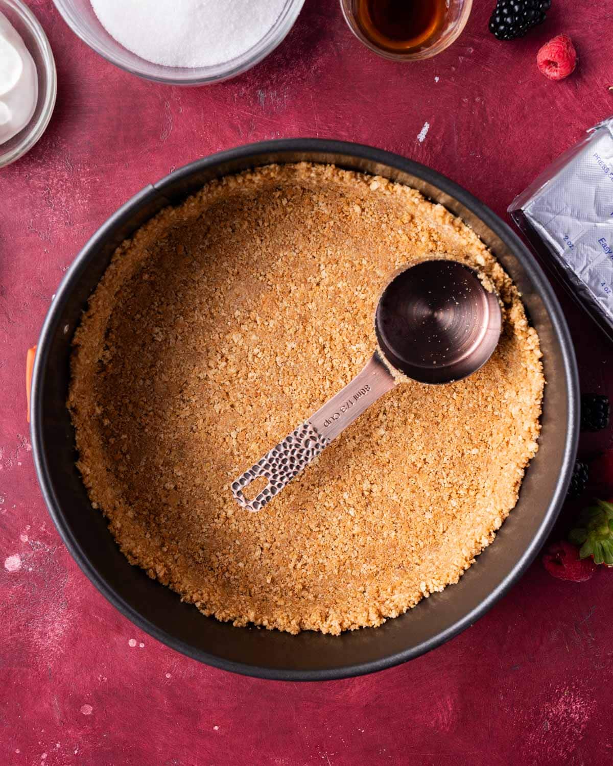 a measuring cup pressing graham cracker crumbs into a springform pan