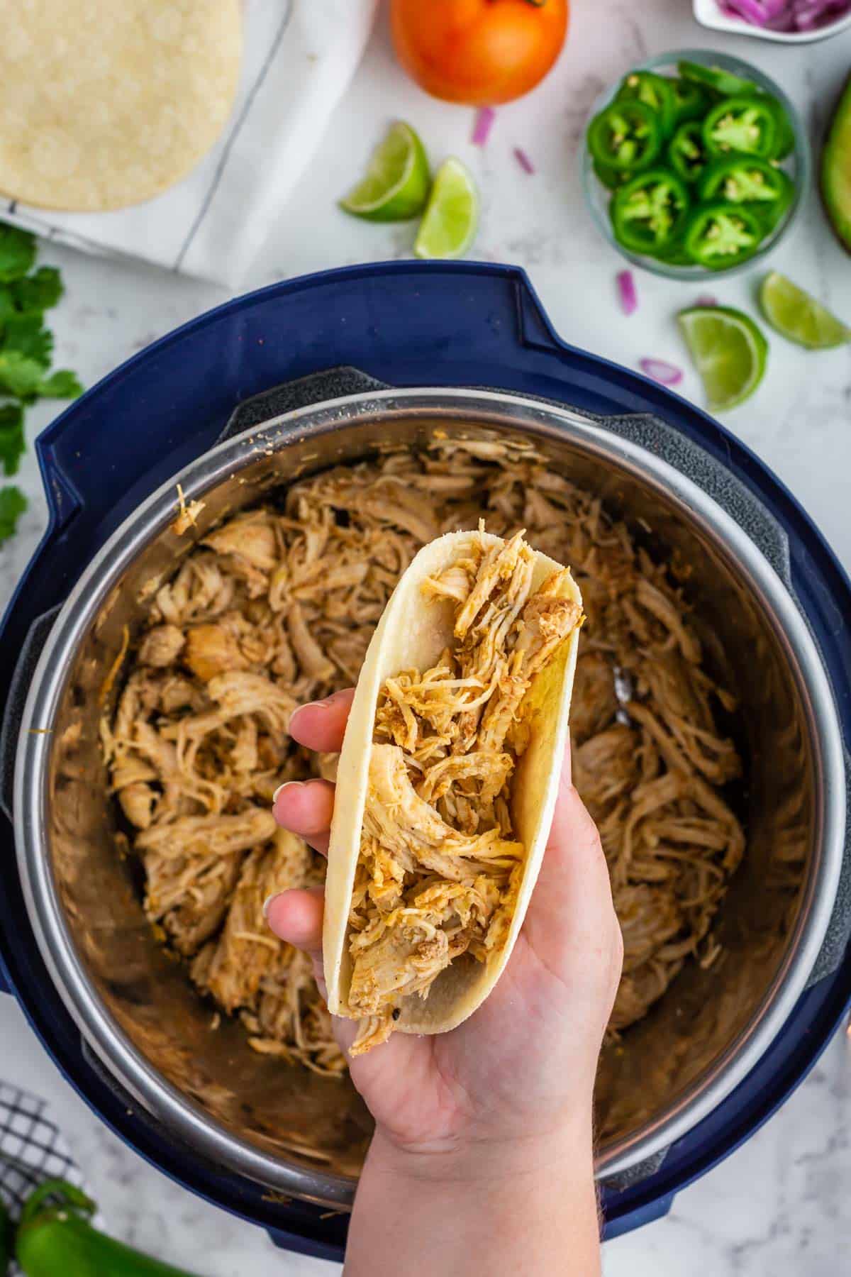 a hand holding a taco filled with salsa verde chicken