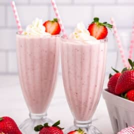 two strawberry milkshakes sitting on a table with straws