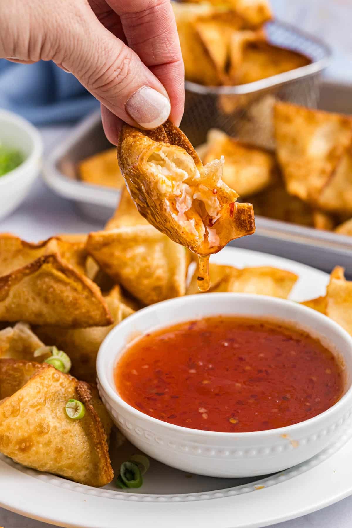 dipping a crab rangoon into red sauce