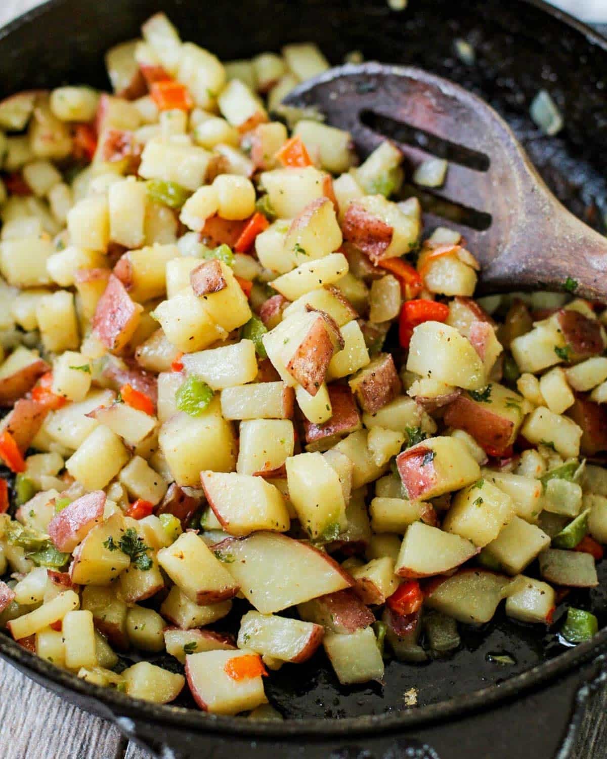 breakfast potatoes in a skillet with a wooden spoon