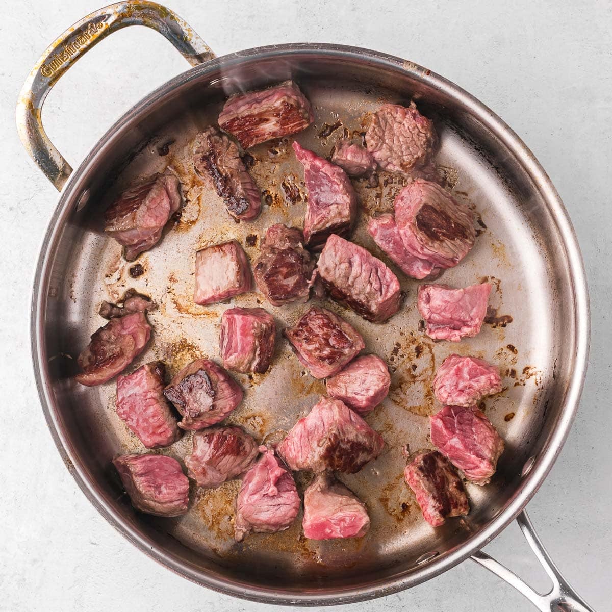 beef cubes searing in a skillet