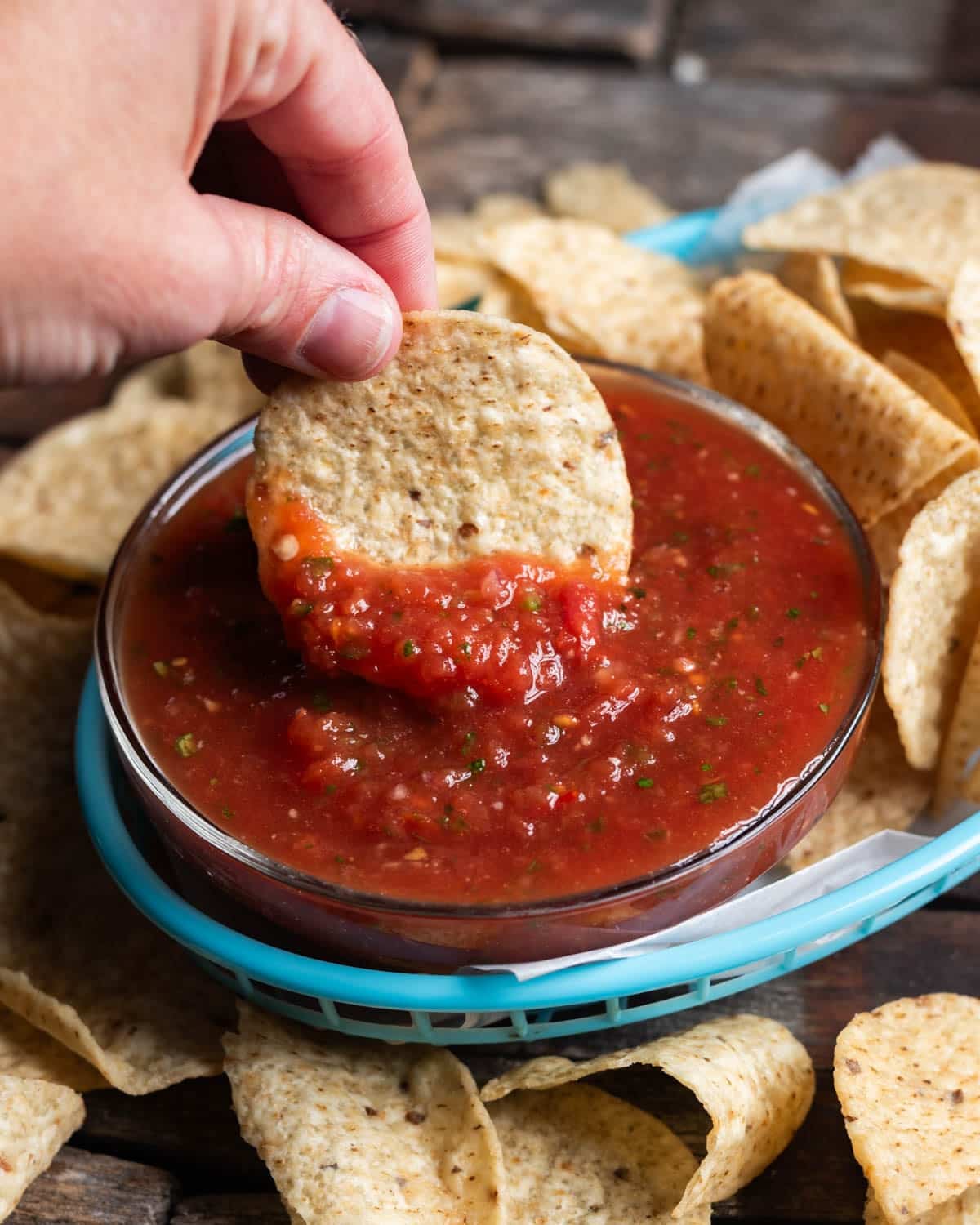 a hand dipping a tortilla chip into salsa