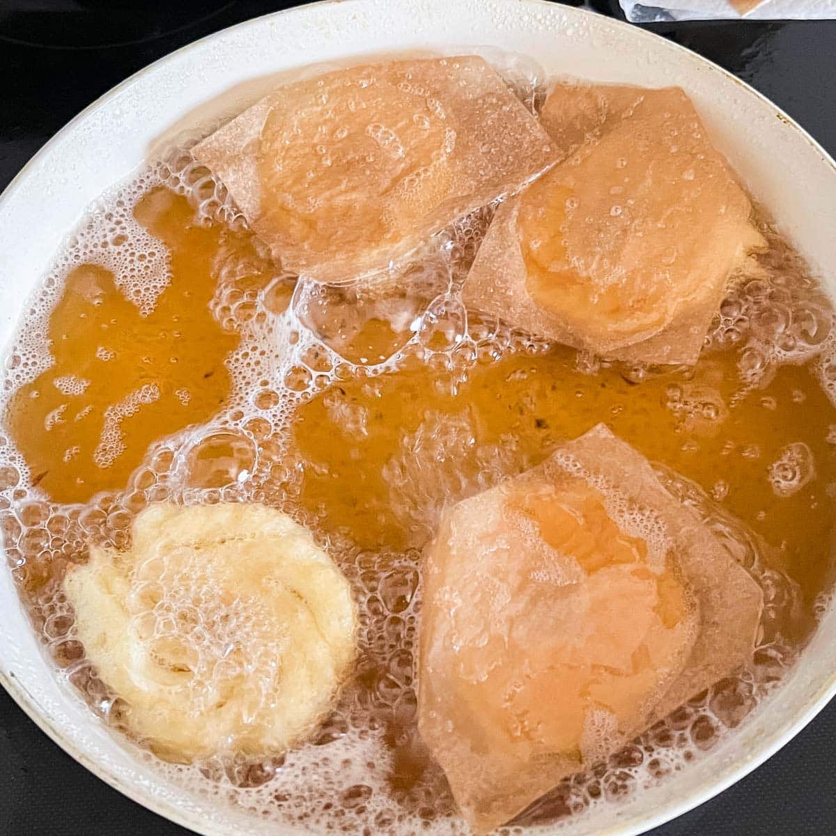 crullers frying in hot oil with parchment paper