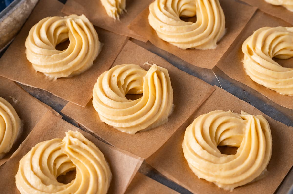 cruller batter piped onto parchment paper squares