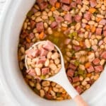 slow cooker ham and beans with a ladle