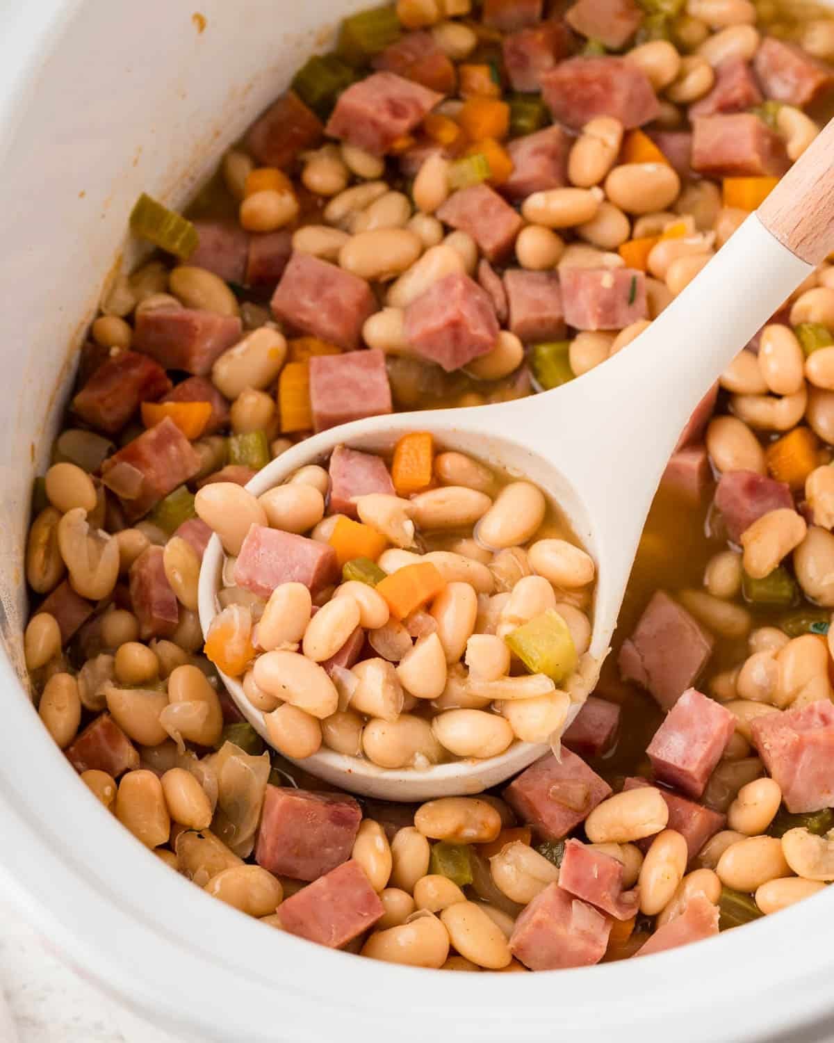 slow cooker ham and beans with a ladle