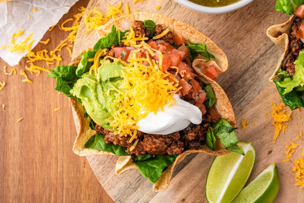 overhead view of a taco salad bowl with avocado, cheddar cheese and sour cream on a table