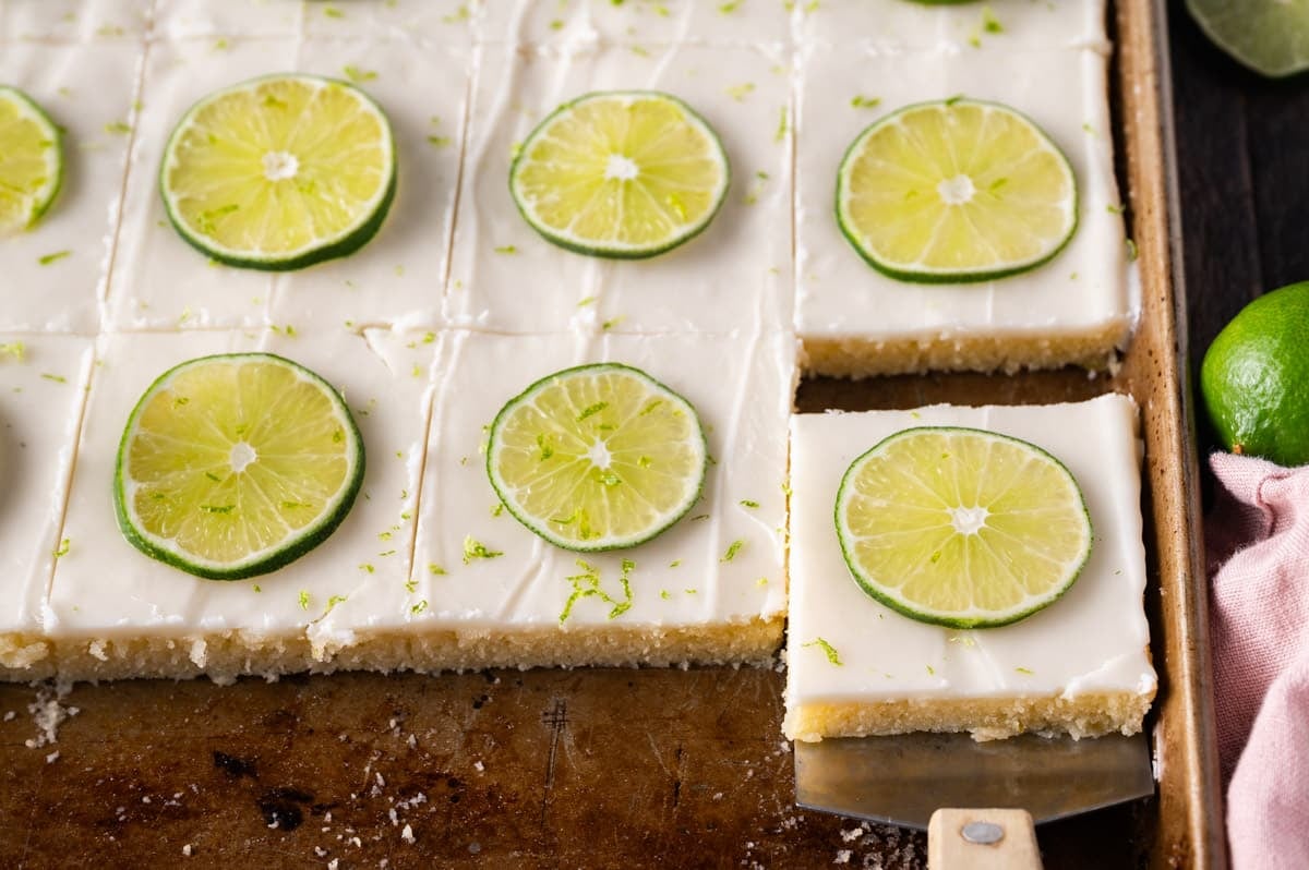 key lime sheet cake in a baking pan with one piece on a spatula