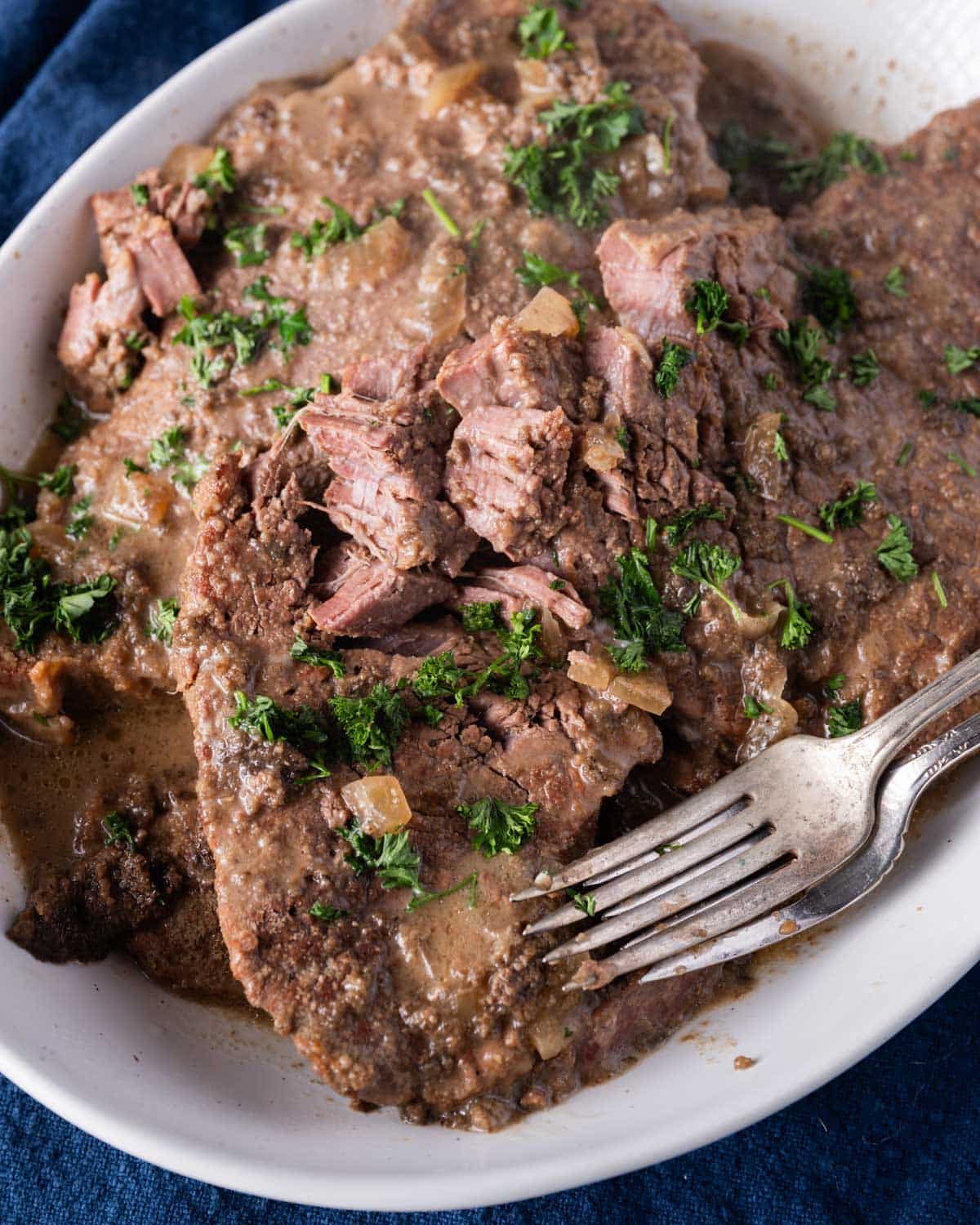 fork tender swiss steak with mushroom sauce on a plate with two forks