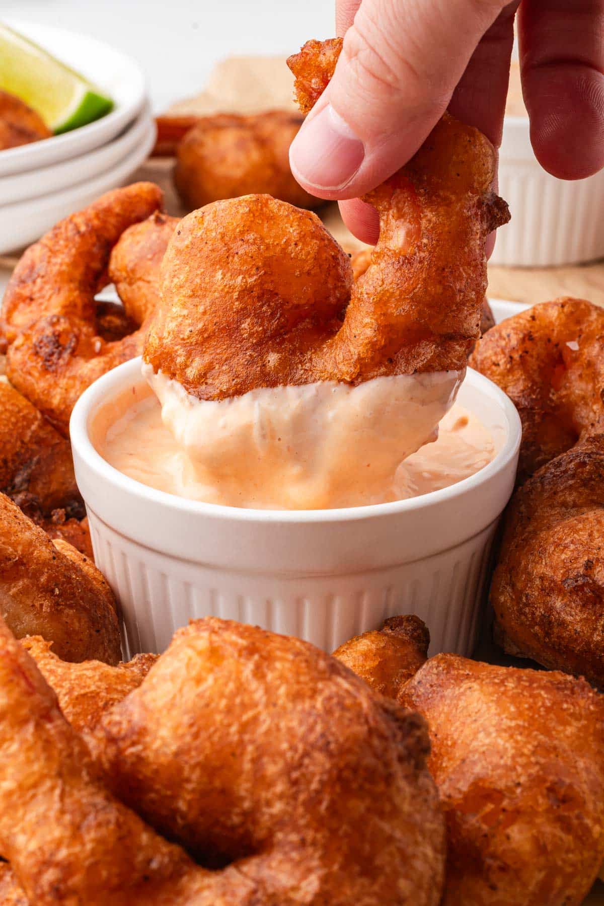 a hand dipping fried shrimp in a chipotle lime sauce