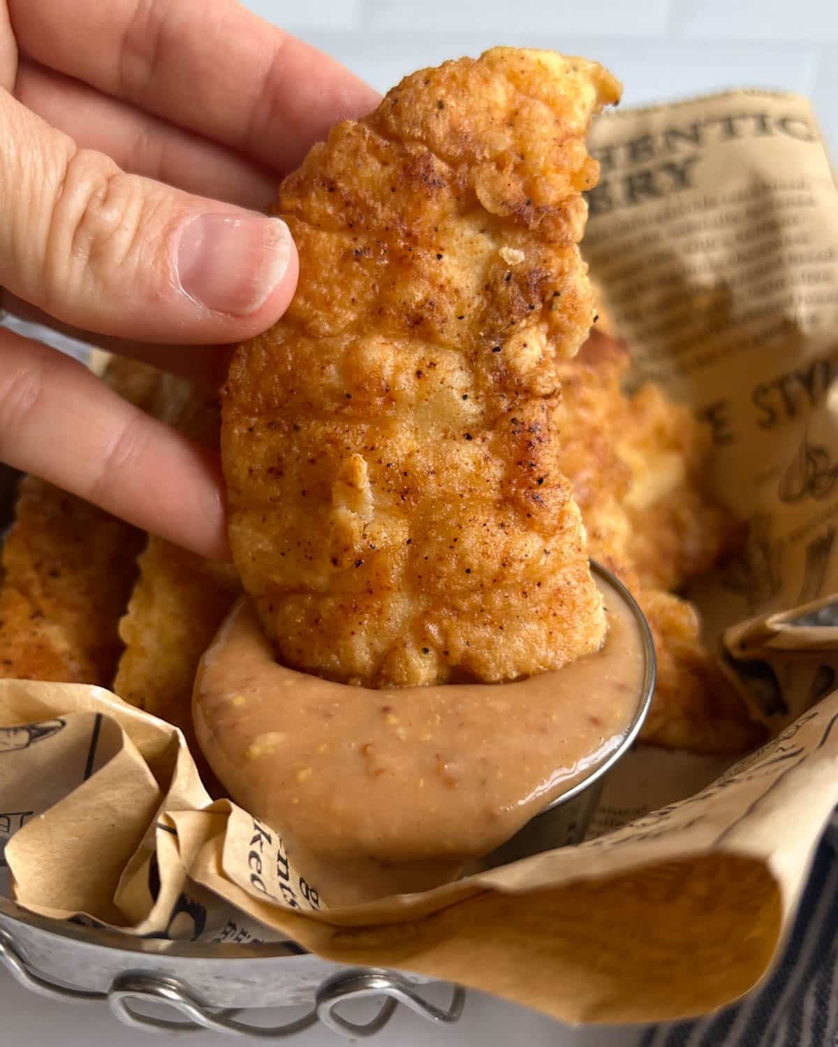 a hand dipping a chicken tender into sauce