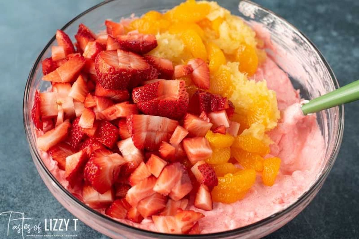 strawberries, oranges and pineapple over jello mixture in a bowl