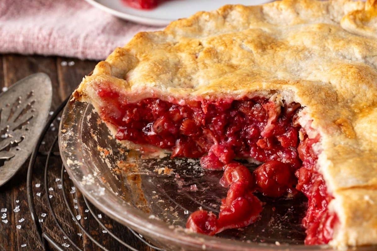 closeup of sour cherry pie in a pan with one slice missing