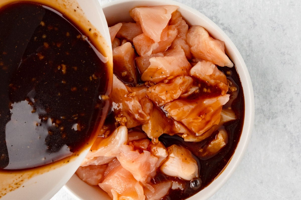 pouring marinade over diced chicken