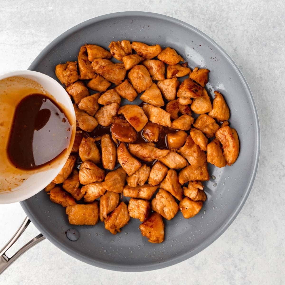 pouring sauce over cooked chicken in a skillet