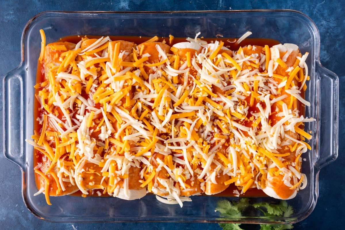 unbaked enchiladas with cheese on top in a baking pan