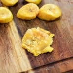 sliced plantains on a cutting board, one smashed