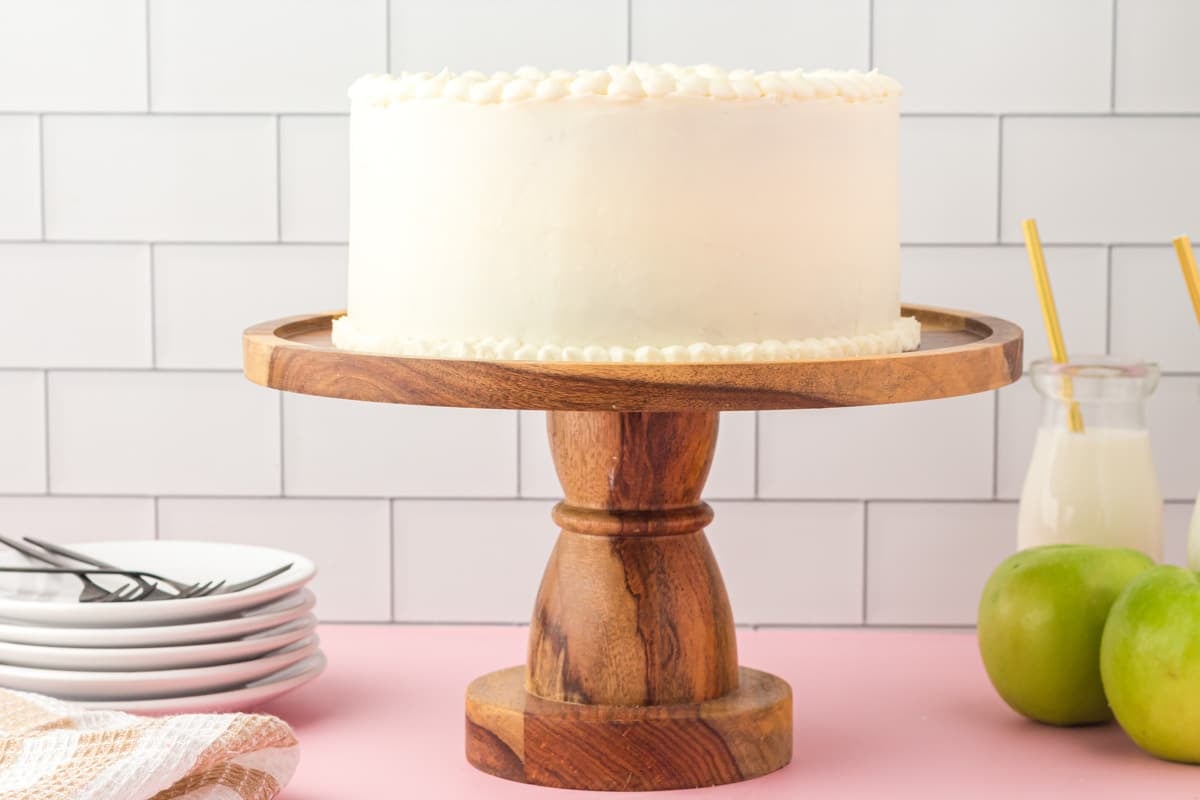 a white frosted cake on a wooden cake stand