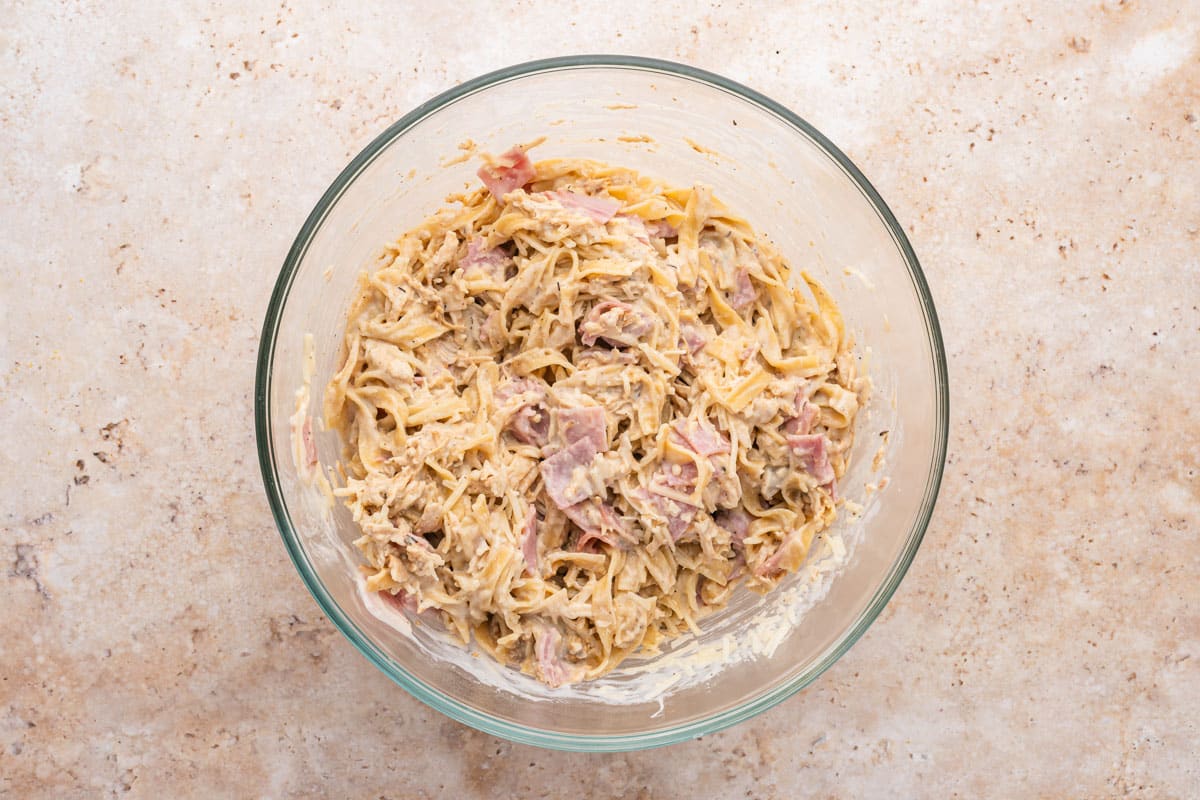 pasta, ham and chicken mixed with creamy sauce in a glass bowl
