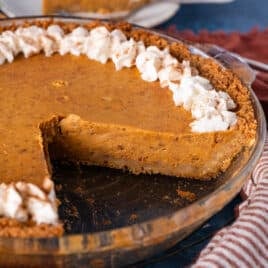 pumpkin pie with graham cracker crust on a table with a slice out