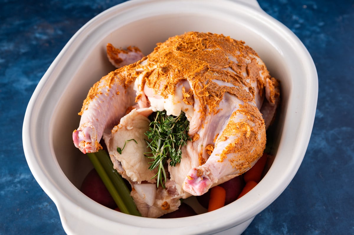 a whole chicken with butter rubbed on top in a slow cooker