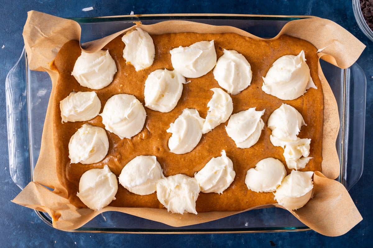 unbaked pumpkin cake with cream cheese frosting dolloped on top