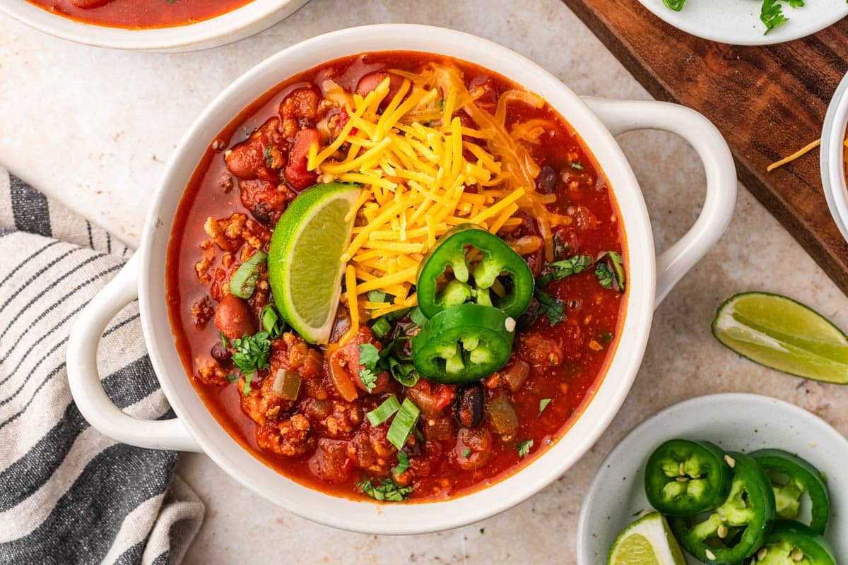 a bowl of ground turkey chili with cheese, pepper and lime on top