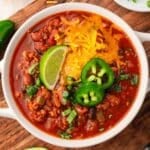 a bowl of ground turkey chili with cheese, pepper and lime on top