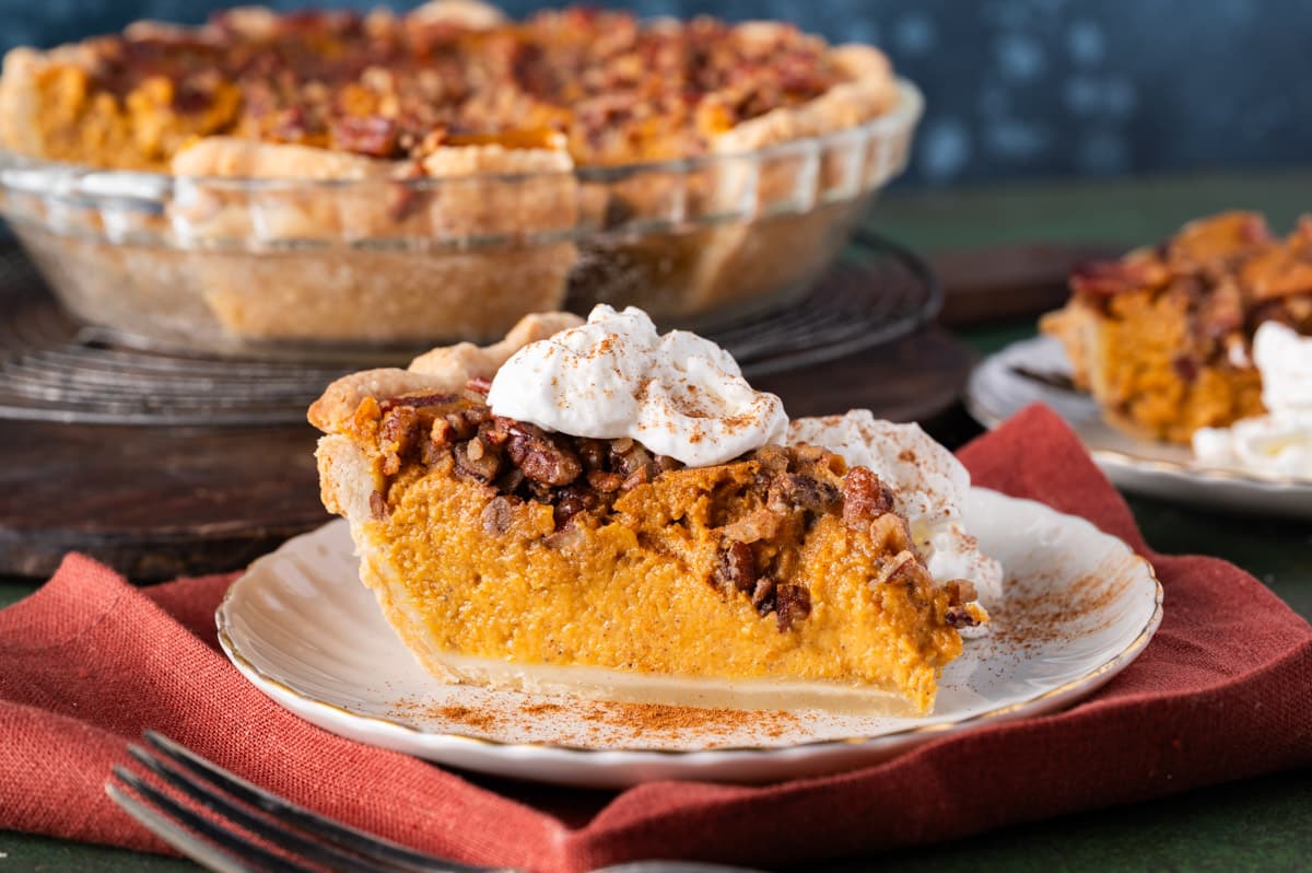 a piece of pumpkin pie with pecans and whipped cream on a table