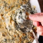 a hand dipping a chip into spinach artichoke dip