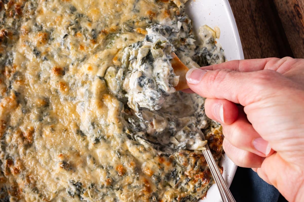 a hand dipping a chip into spinach artichoke dip