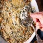 a hand dipping a chip into spinach artichoke dip