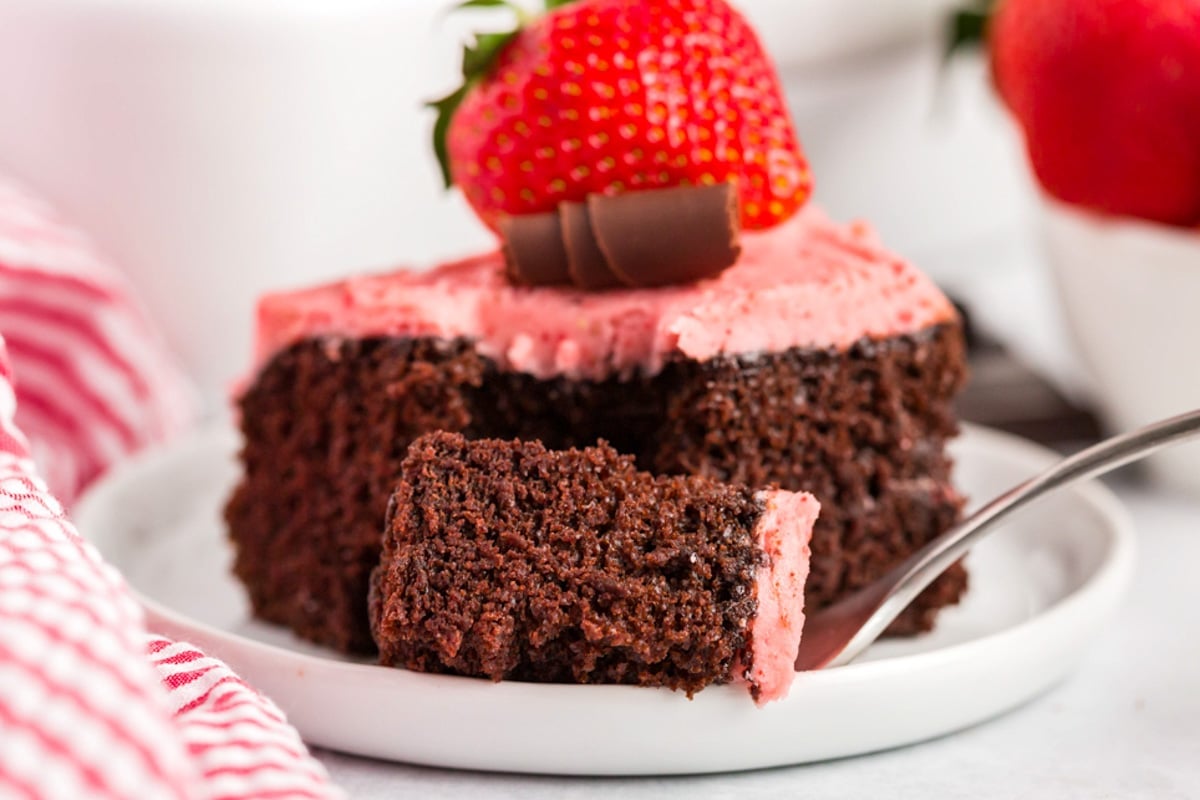 a piece of chocolate strawberry cake on a plate with one bite cut