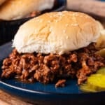 a sloppy joe sandwich on a plate with pickles and chips