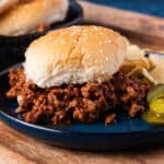 homemade sloppy joes on a plate with pickles and chips
