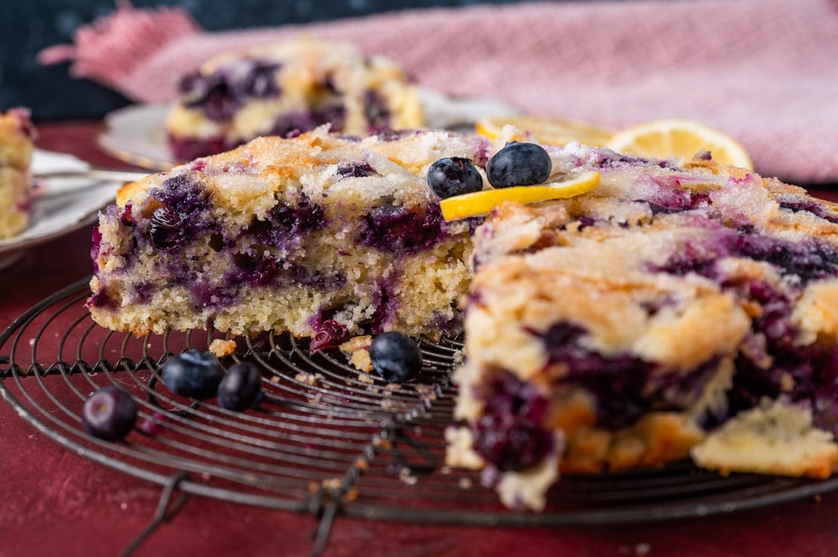 lemon blueberry cake on a wire rack with a piece cut out