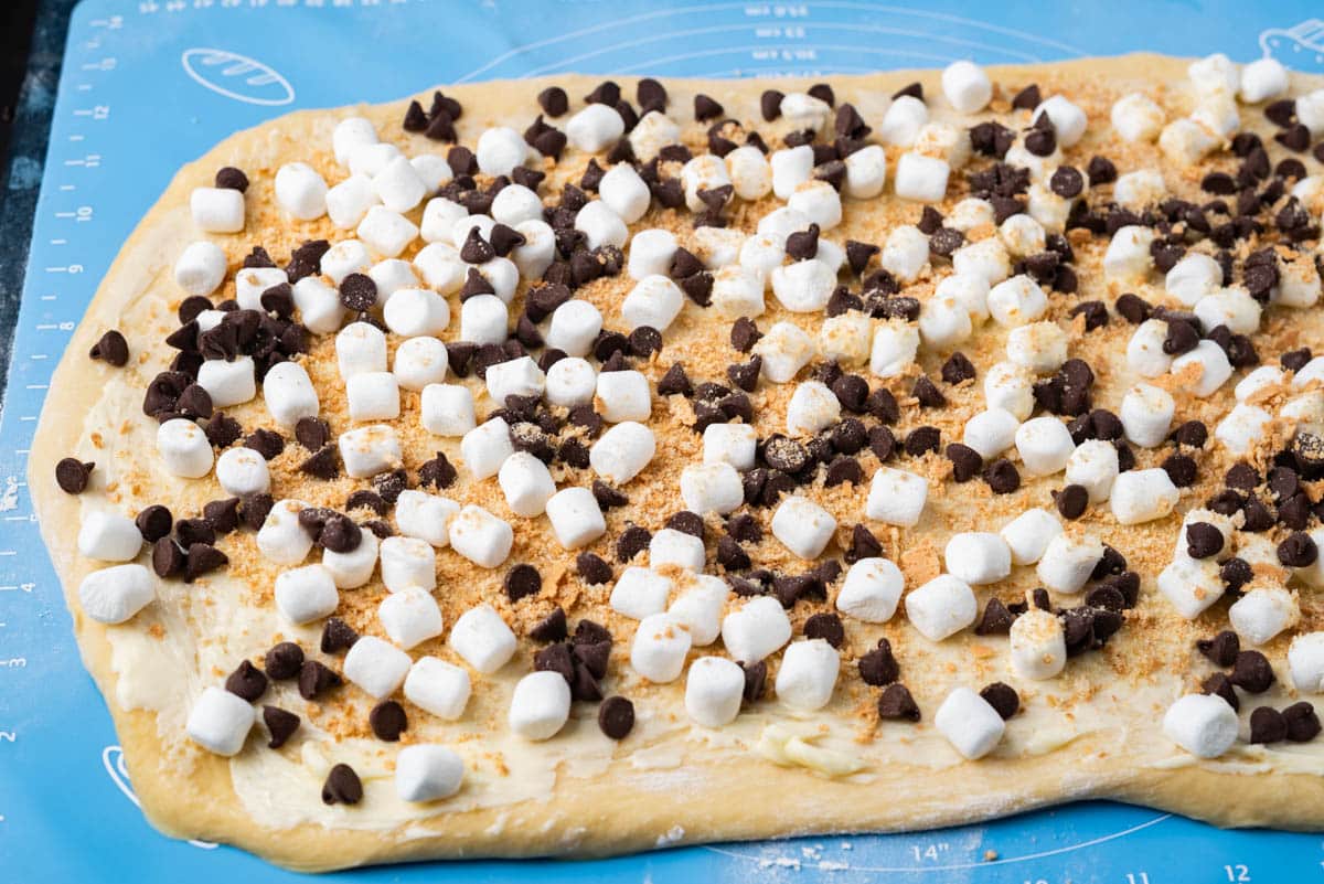 dough rolled out with marshmallows, chocolate chips and graham crackers on top