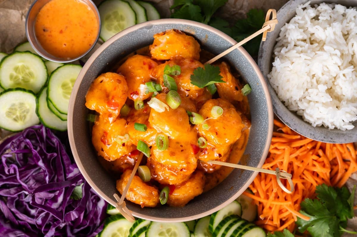 a bowl of bang bang shrimp in a bowl with veggies around it