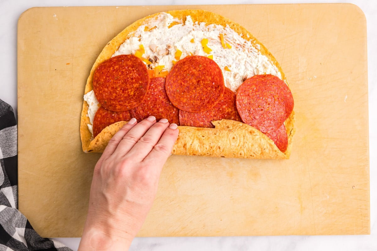 a hand rolling up a tortilla with pepperoni